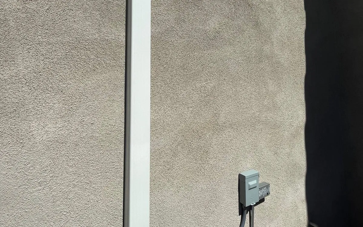 A white line-set cover running up the stucco wall above the disconnect.