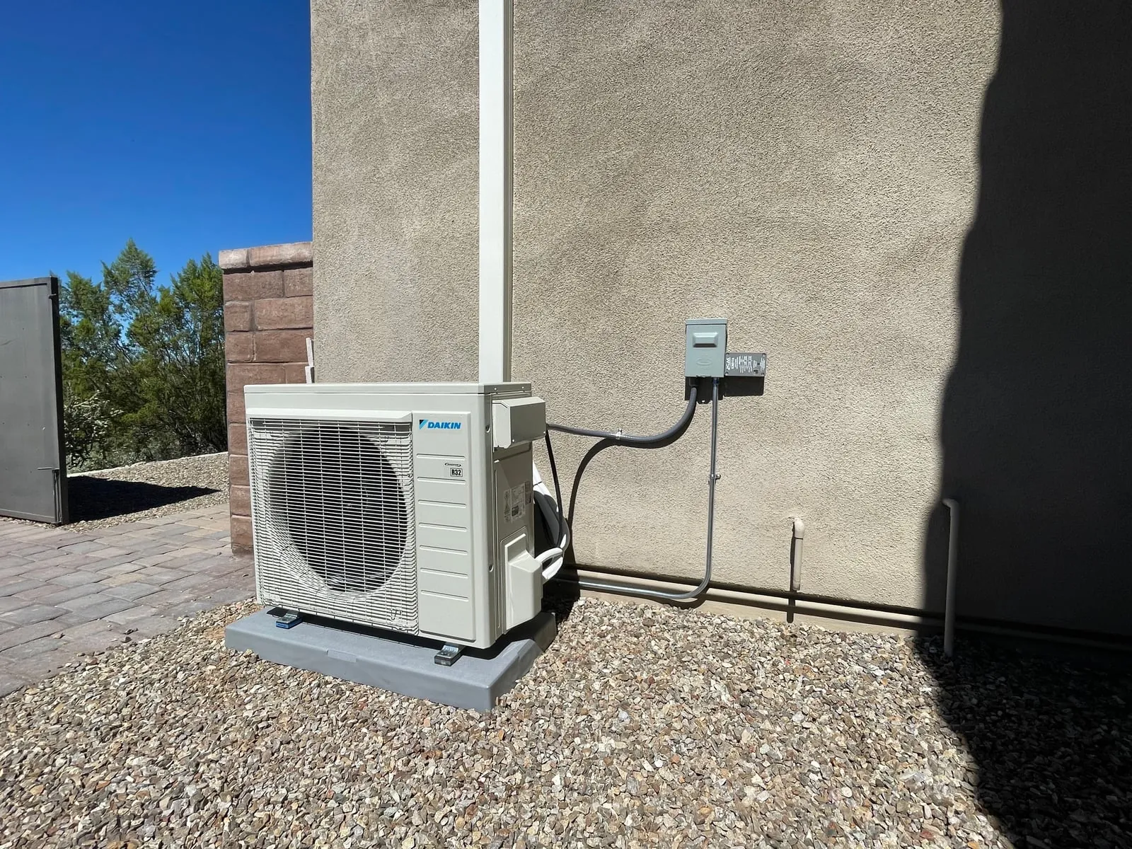 The new ductless outdoor unit on its pad, with the covered line set running up the wall and a disconnect beside it.