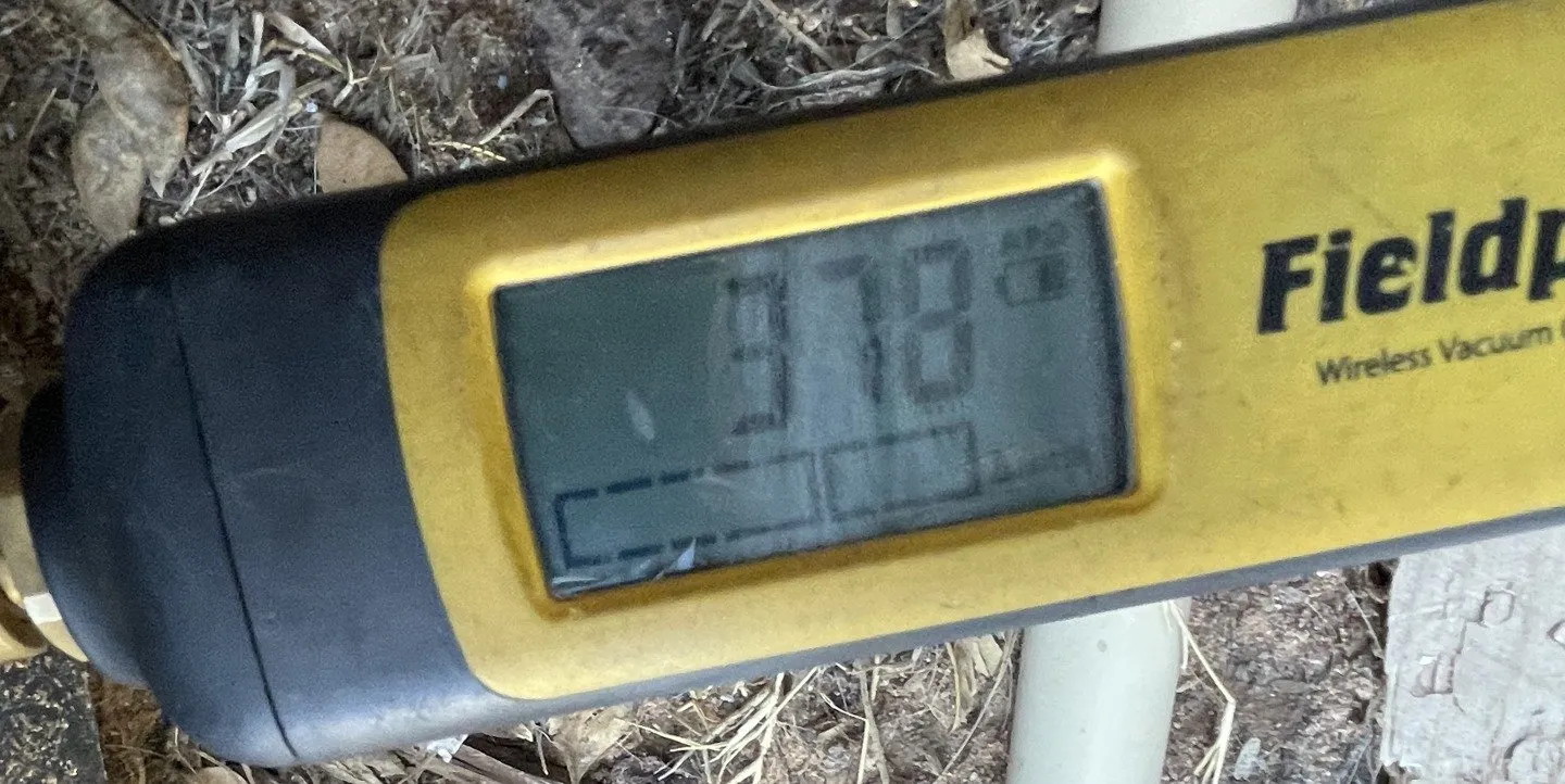 A micron gauge clipped to the refrigerant line, showing a low vacuum reading during evacuation.