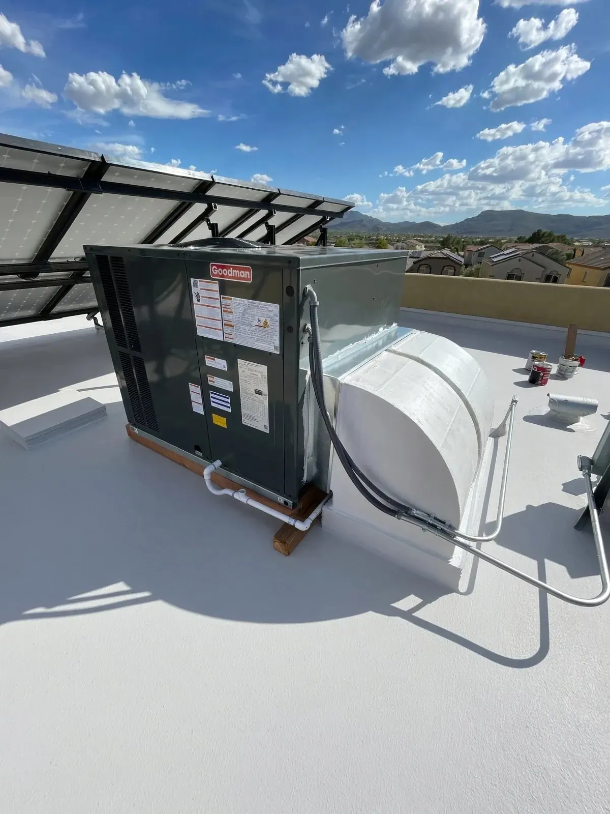 The new gas/electric package unit on its sleepers on a white-coated flat roof, with the coated duct transition beside it and the mountains behind.