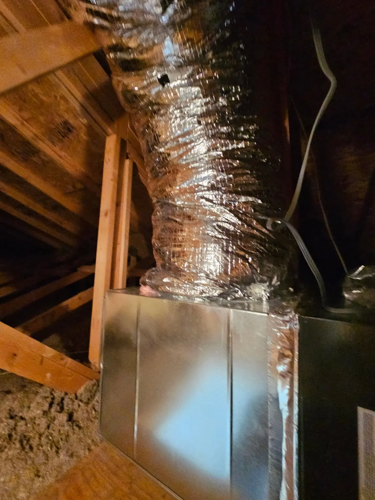 Insulated flexible duct joined to a new sheet-metal fitting at the equipment in the attic.