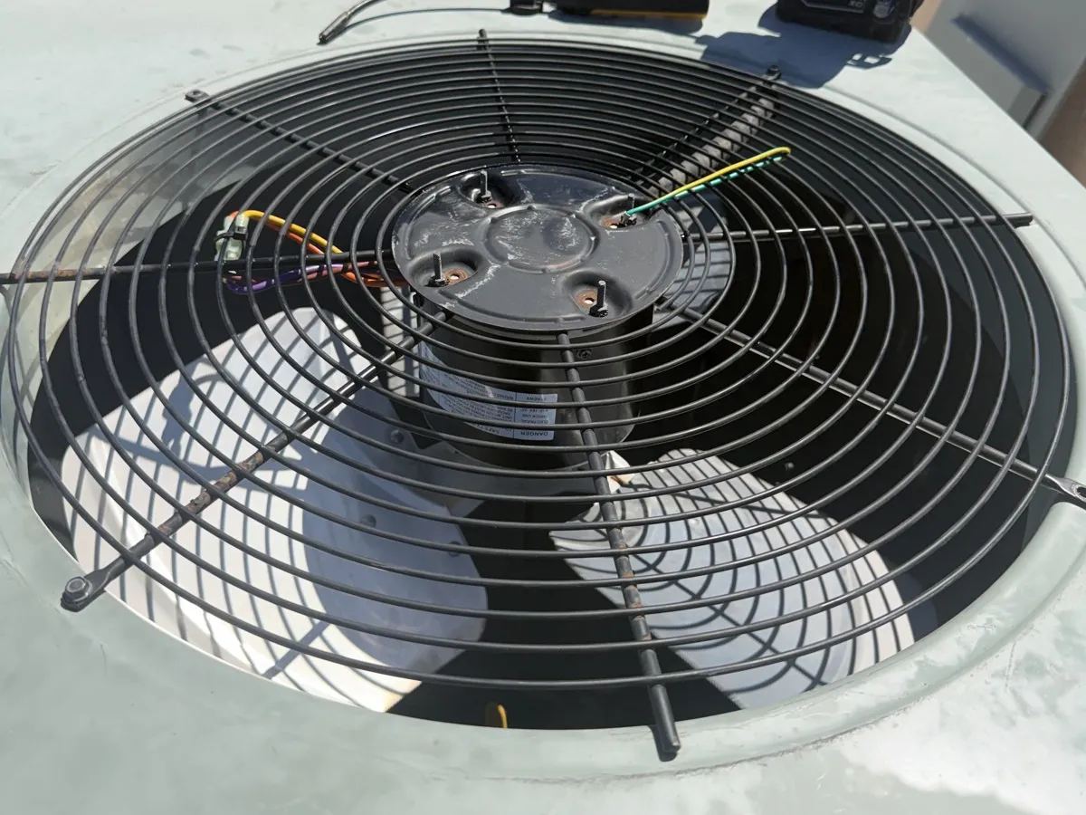 The outdoor fan grille and motor hub on top of the rooftop gas-pack unit during the motor replacement.