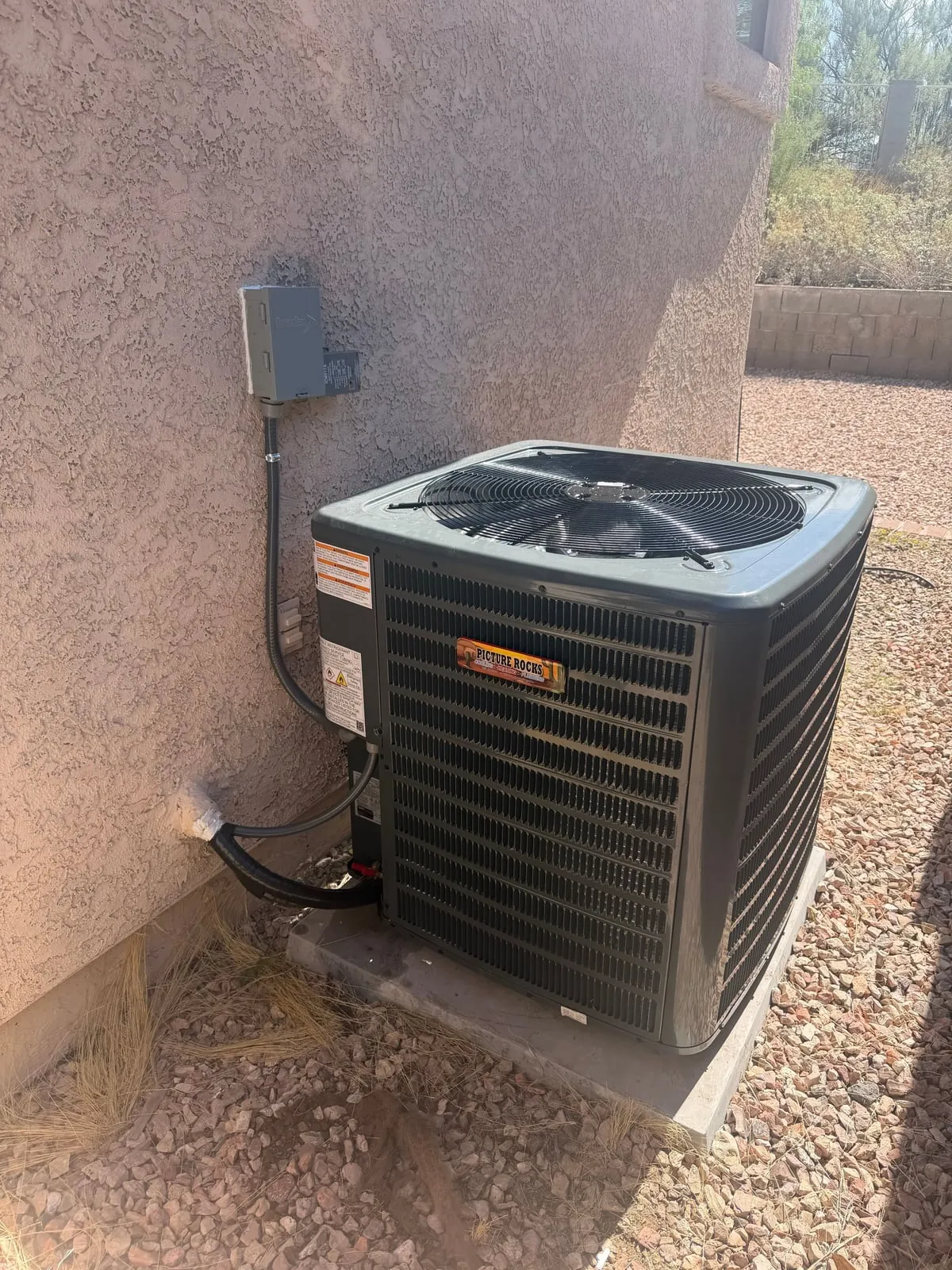 The new outdoor AC unit on its pad beside the stucco wall, with its disconnect mounted above it.