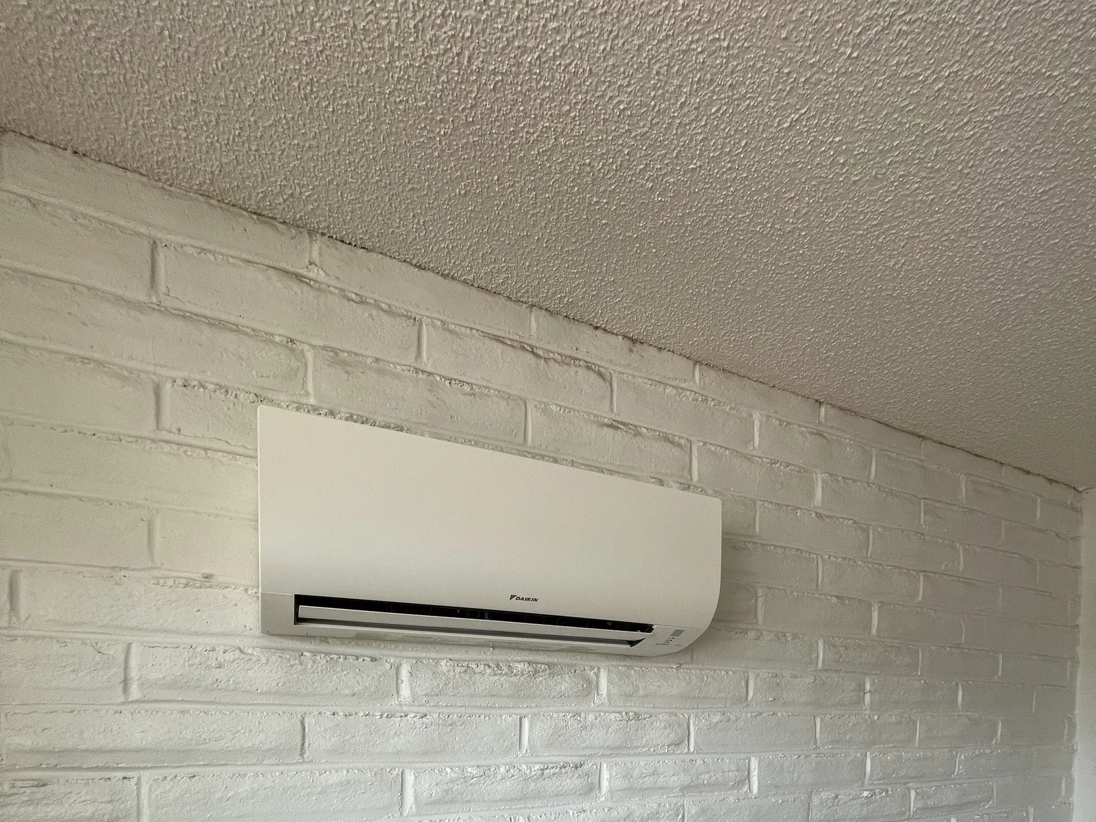 Finished wall-mounted ductless head on a painted brick wall.