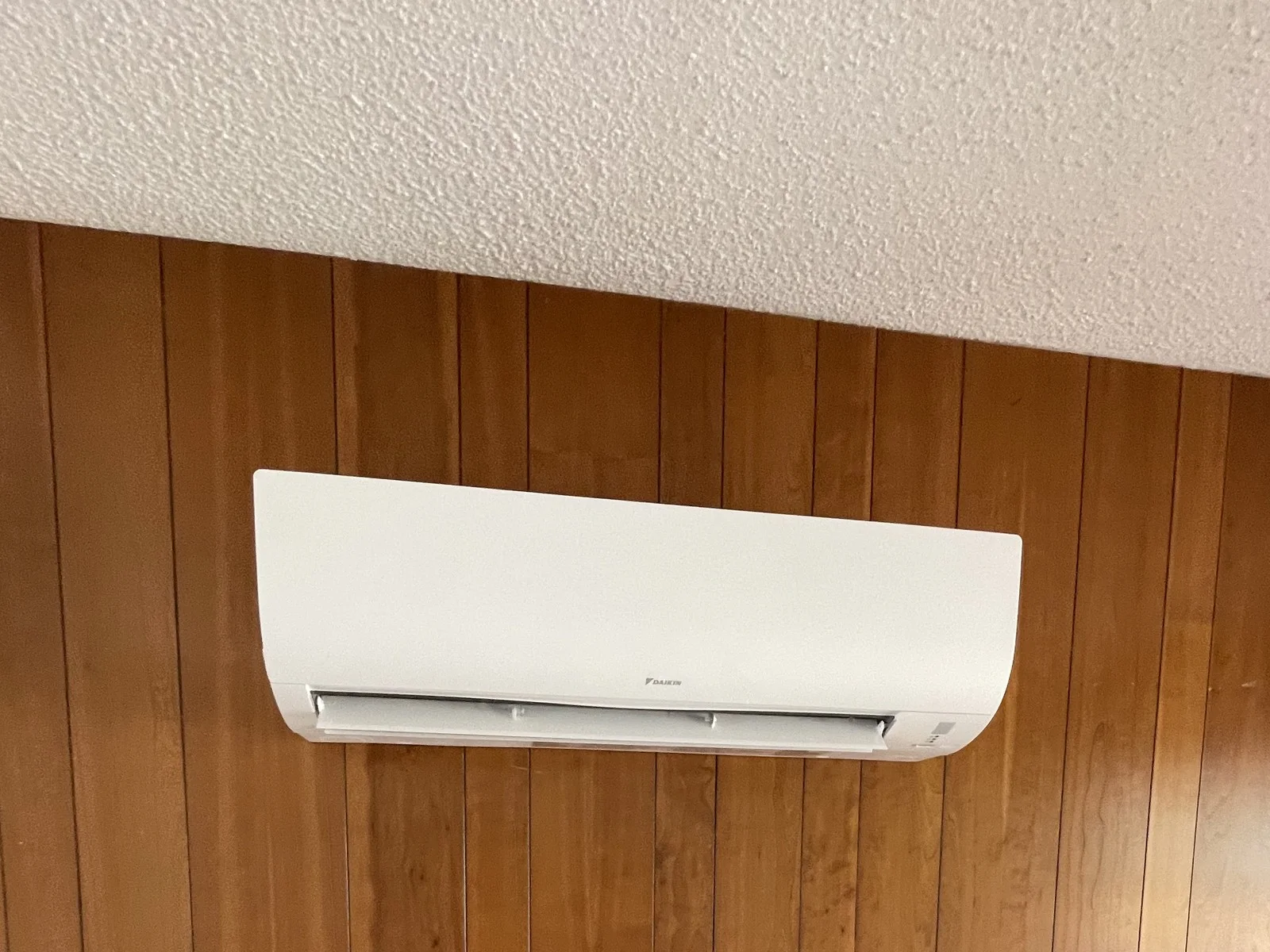A finished wall-mounted ductless head on wood paneling.